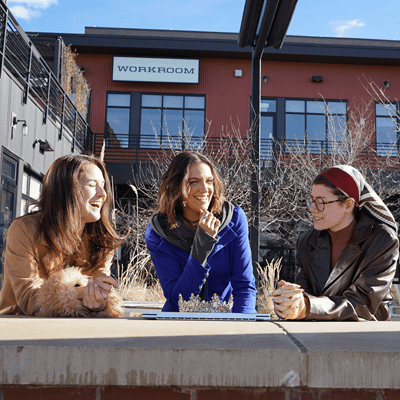 Three women outside an industrial building laughing at a work meeting